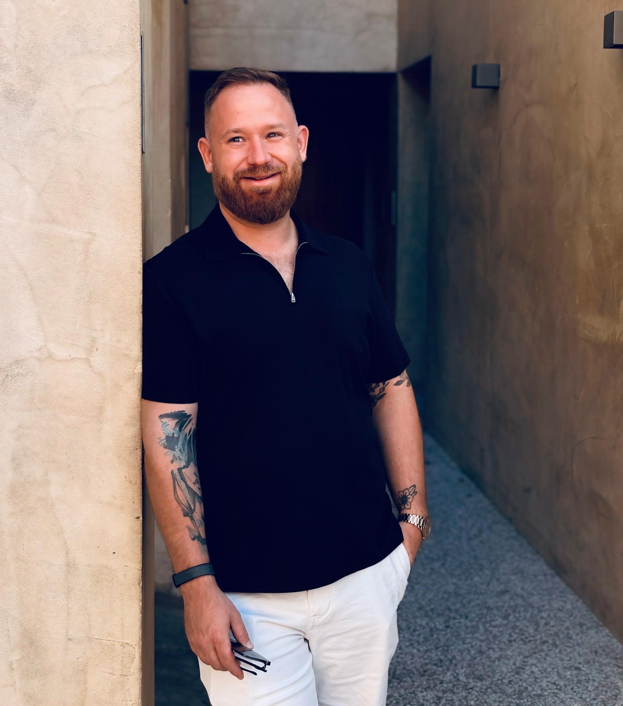 Dom Kozak leaning against a sandstone wall in a narrow courtyard, smiling